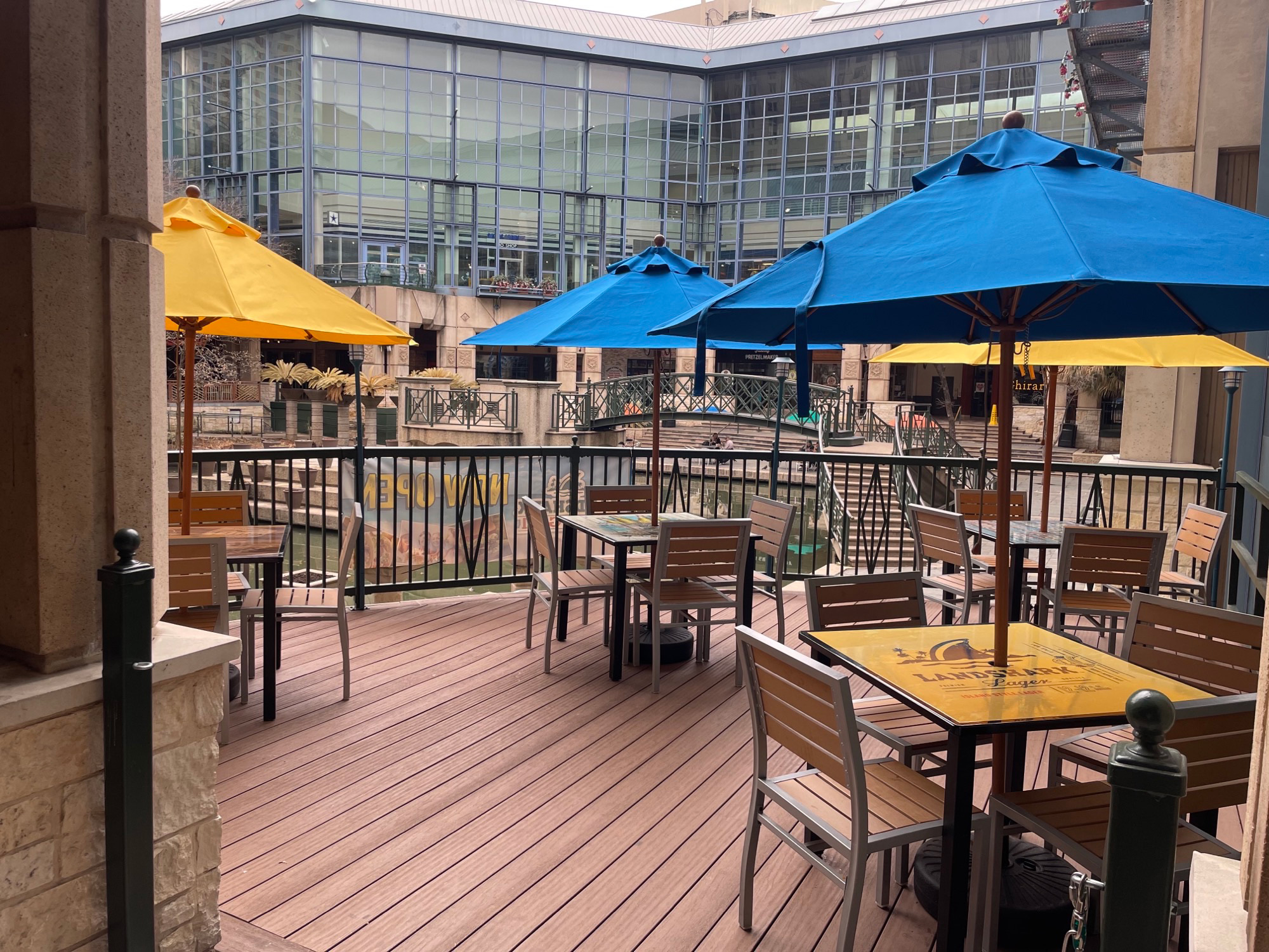 Tables and chairs with umbrellas on the wood deck with a small bridge in the background